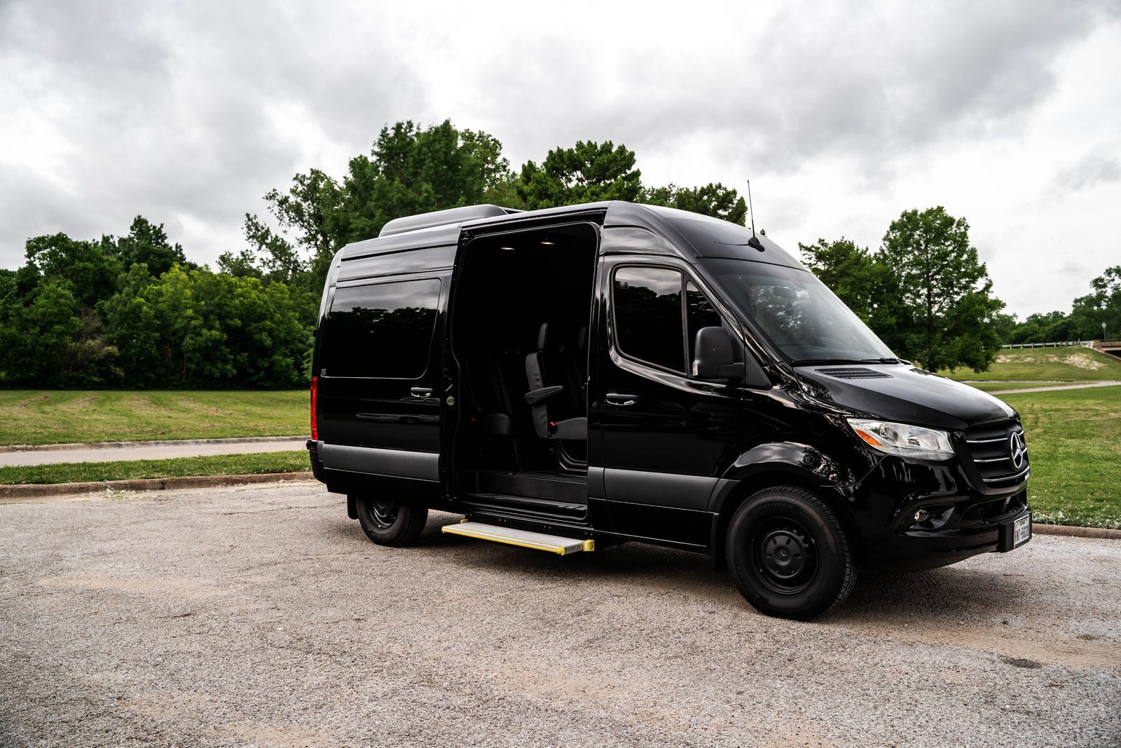 Black Passenger Sprinter with side door open, parked near green trees