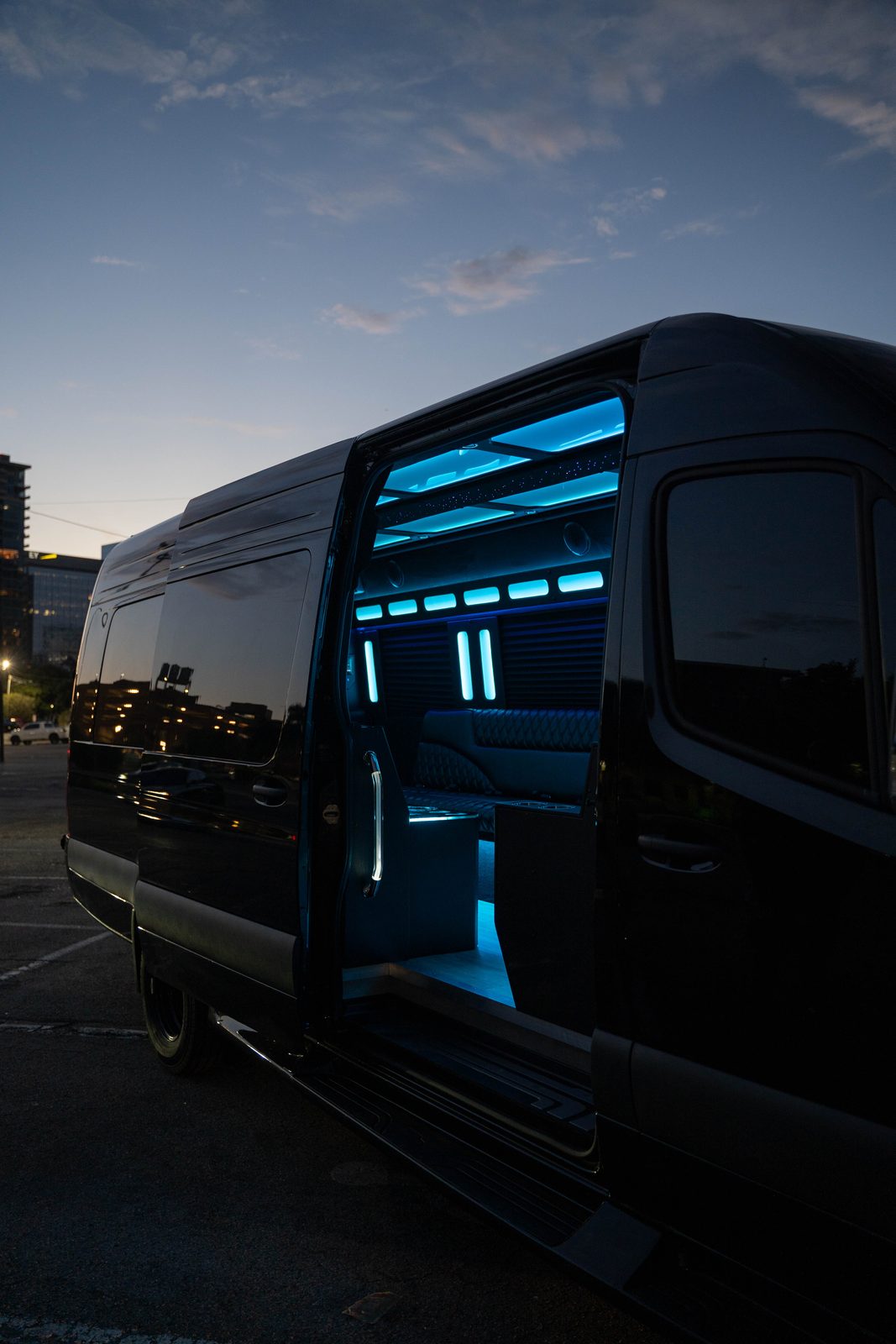 Passenger Sprinter side door open at dusk showing the blue-lit interior